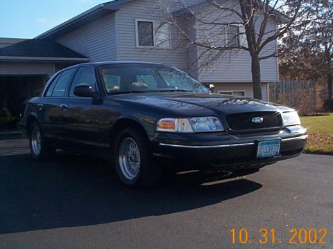 1998 Ford Crown Victoria - A black 1998 Ford Crown Victoria is parked in front of a house on a sunny day.
