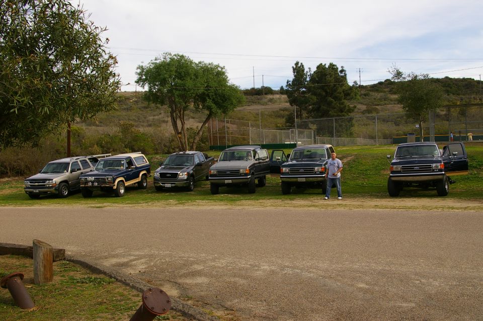 Dark blue Ford Bronco with a white camper shell, parked in a line with other vehicles