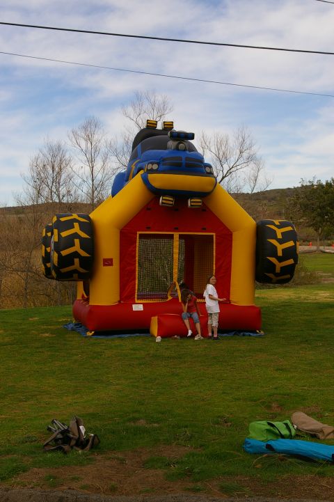 1986 Ford Bronco - An inflatable bounce house designed to look like a monster truck sits on a grassy field under a cloudy sky.