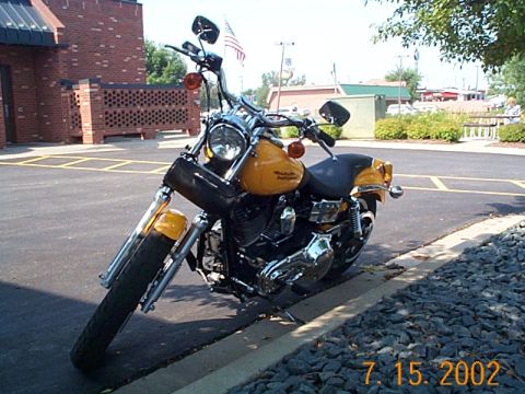 1998 Ford Crown Victoria - A yellow motorcycle is parked on the side of a road with a brick building in the background.