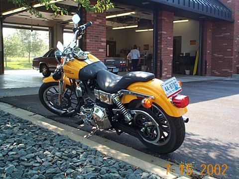 1998 Ford Crown Victoria - A yellow motorcycle is parked outside a garage, with a brown car visible inside.