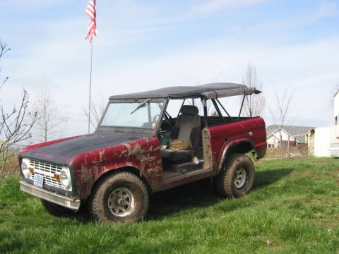 1968 Ford Bronco - A muddy 1968 Ford Bronco with a soft top sits in a grassy field under a blue sky.