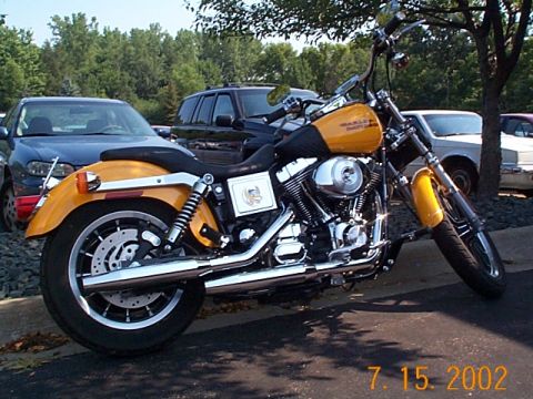 1998 Ford Crown Victoria - A yellow Harley-Davidson motorcycle is parked outdoors next to several cars.