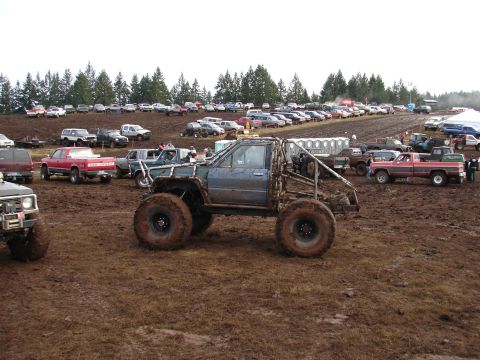 1996 Ford Bronco - A heavily modified truck with a roll cage sits in the mud at a mud bogging event, with many other vehicles parked in the background.