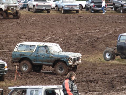 1996 Ford Bronco - Muddy 1978 Ford Bronco at an off-road event. Multiple trucks are present in the muddy terrain.