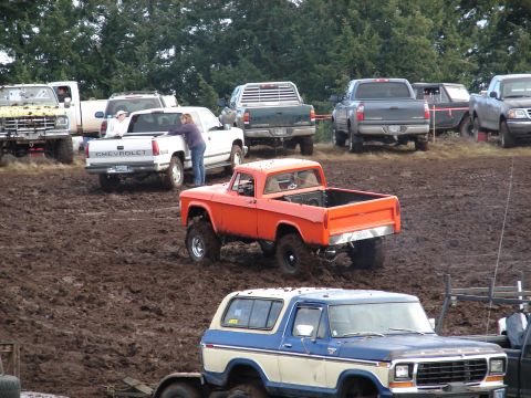 1996 Ford Bronco - An orange pickup truck navigates a muddy track alongside other vehicles.
