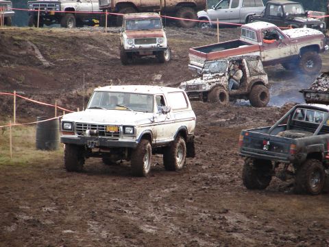 1996 Ford Bronco - White Ford Bronco navigates a muddy off-road course with other vehicles present.