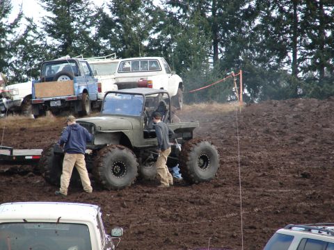 1996 Ford Bronco - Several off-road vehicles are gathered in a muddy area, with people attending to a heavily modified jeep.