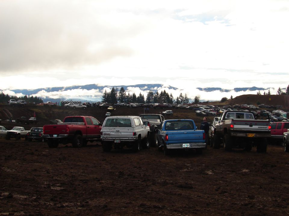 Muddy field with many trucks and SUVs parked under cloudy skies