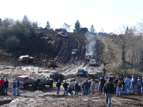 1996 Ford Bronco - Spectators watch as multiple off-road vehicles navigate a muddy hill during an event.