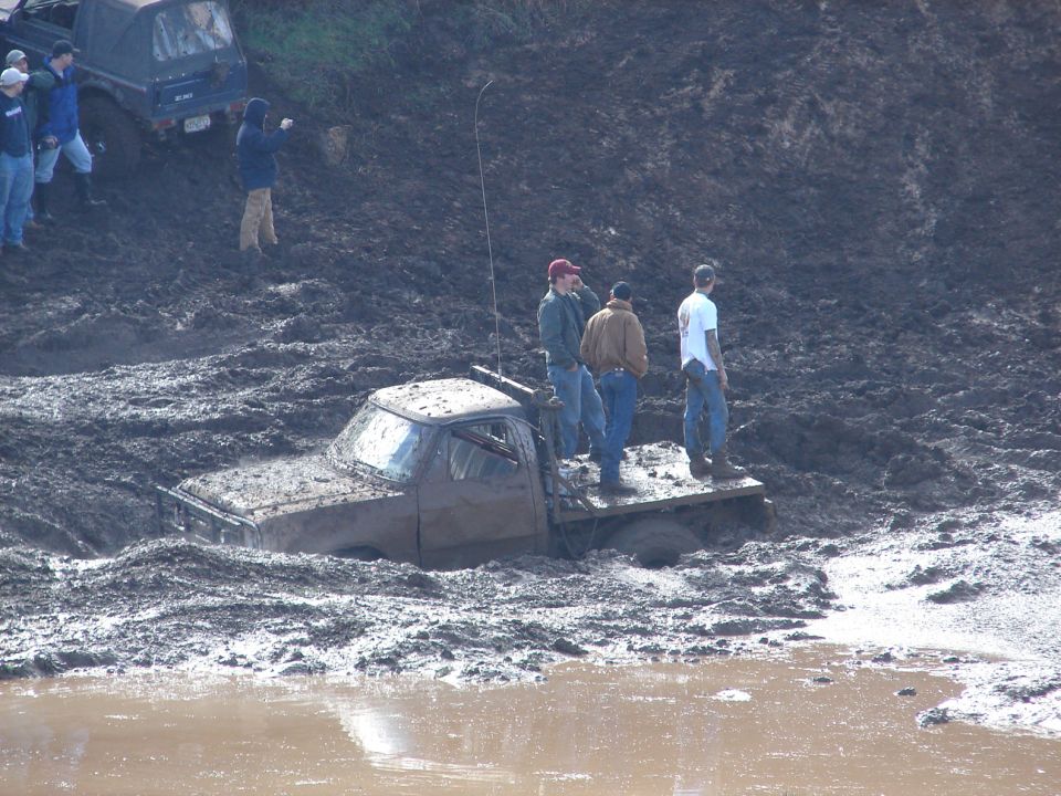 Truck stuck deep in mud with people standing on its bed
