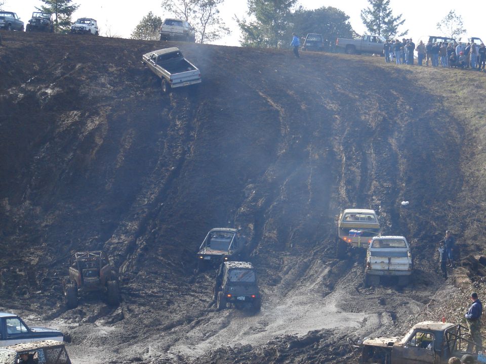 Several trucks and SUVs driving up a muddy hill. Some are stuck