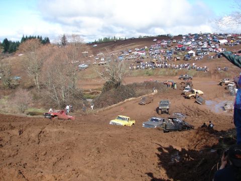 1996 Ford Bronco - A large gathering of vehicles are stuck in a muddy field during an event, with spectators watching from a hillside.