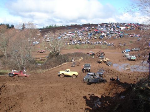 1996 Ford Bronco - A large crowd watches as numerous off-road vehicles navigate a muddy terrain during an event.