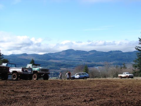 1996 Ford Bronco - Several trucks and a station wagon are parked in a muddy field with hills in the background.