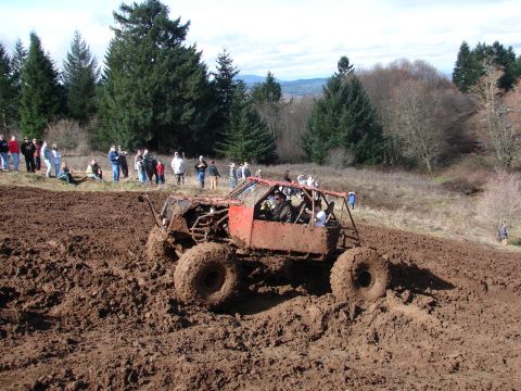 1996 Ford Bronco - A custom-built off-road buggy churns through thick mud during an event, observed by a crowd of onlookers.