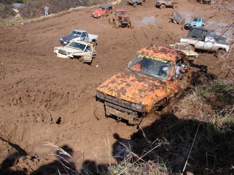 1996 Ford Bronco - Several vehicles are bogged down in thick mud at an off-road event.