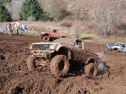 1996 Ford Bronco - Multiple trucks navigate a muddy off-road course during an event.