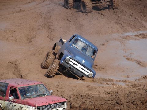 1996 Ford Bronco - A blue 1956 Ford F-100 pickup truck navigates a muddy terrain, with another vehicle visible in the foreground.