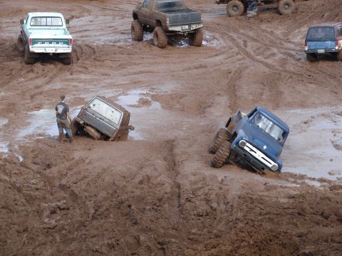 1996 Ford Bronco - Multiple trucks are stuck in a muddy off-road event.