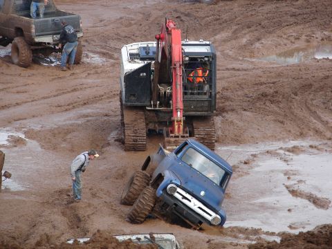1996 Ford Bronco - A blue pickup truck is deeply stuck in a mud pit, with an excavator and other vehicles present.