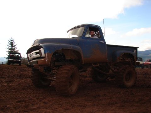 1996 Ford Bronco - A lifted blue pickup truck navigates a muddy terrain with other vehicles present.