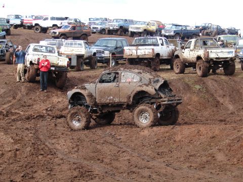 1996 Ford Bronco - Multiple off-road vehicles are gathered in a muddy field, with a heavily modified Volkswagen Beetle in the foreground.