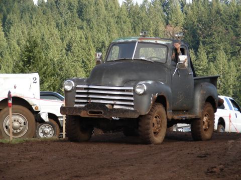 1996 Ford Bronco - This vintage black pickup truck, likely from the 1950s, navigates a muddy terrain alongside other vehicles.