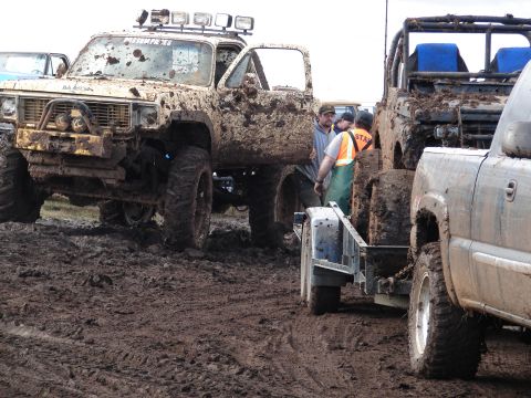 1996 Ford Bronco - Several heavily mud-covered off-road vehicles are parked in a muddy area, with people gathered near one of them.