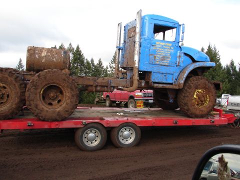 1996 Ford Bronco - A muddy blue semi-truck is transported on a flatbed trailer, with a red pickup truck visible in the background.