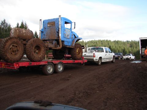 1996 Ford Bronco - A blue truck is loaded onto a trailer, being towed by a white pickup truck through a muddy area.