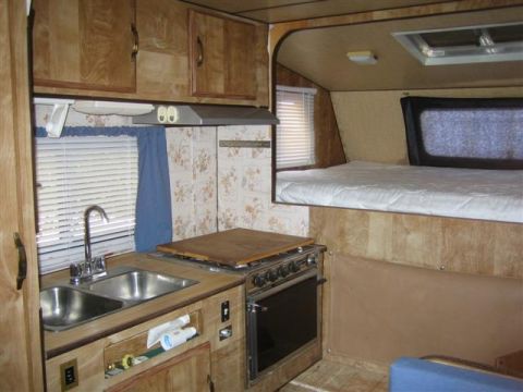 1999 Ford F-250 - The interior of a camper shows a kitchen area with a double sink and stove, and a sleeping area above.
