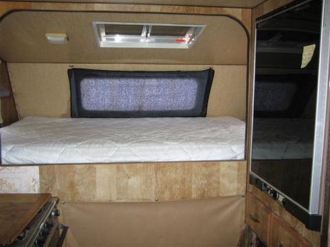1999 Ford F-250 - The interior of a camper shows a bed, wood paneling, and a mirrored cabinet, with a skylight overhead.