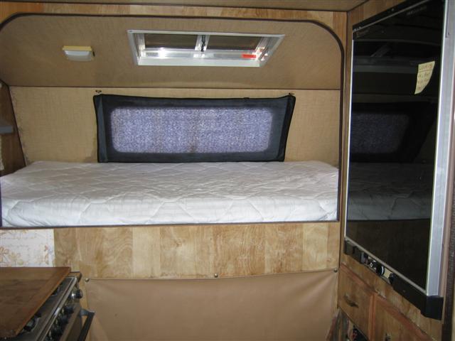 Camper interior with a mattress on a platform, wood paneling, a skylight, and a mirrored cabinet