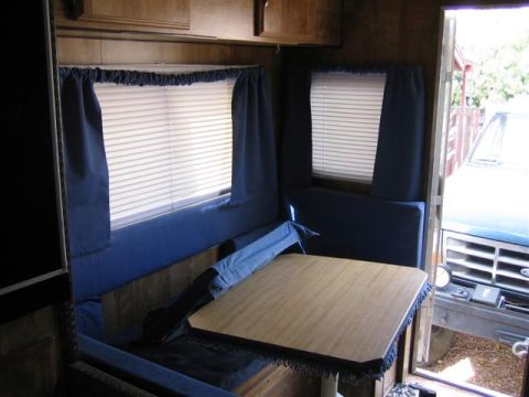 1999 Ford F-250 - The interior of a camper shows blue seating and a wooden table, with a 1999 Ford F-250 visible through the open doorway.