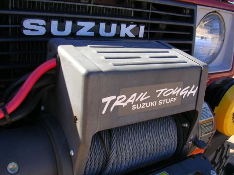 1987 Suzuki Samurai - Close-up of the front of a Suzuki Samurai, highlighting the grille and an aftermarket winch with a 'Trail Tough' sticker.