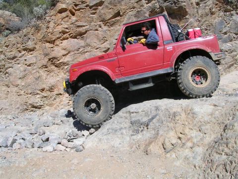 1987 Suzuki Samurai - A red 1987 Suzuki Samurai navigates a steep, rocky trail with a driver at the wheel.