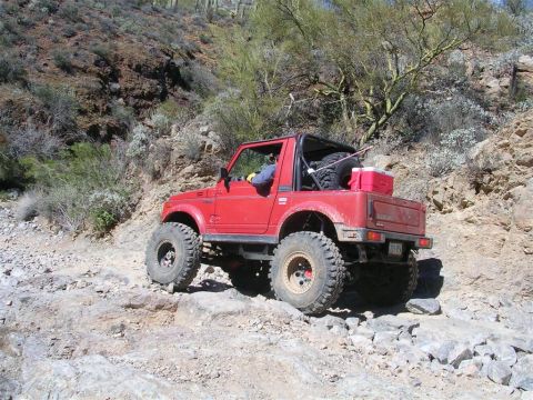1987 Suzuki Samurai - This red 1987 Suzuki Samurai navigates a challenging rocky terrain, its off-road capabilities.