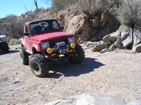 1987 Suzuki Samurai - A red 1987 Suzuki Samurai navigates a rocky off-road trail under a clear blue sky.