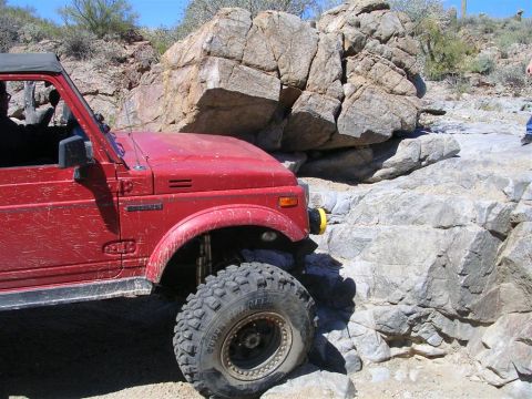 1987 Suzuki Samurai - A red 1987 Suzuki Samurai navigates a rocky trail, demonstrating its off-road capabilities.