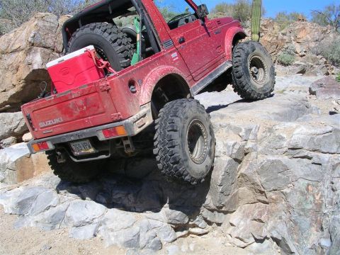 1987 Suzuki Samurai - This red Suzuki Samurai is navigating a rocky trail, its off-road capabilities.