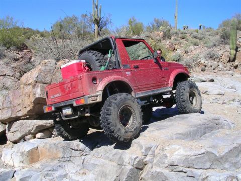1987 Suzuki Samurai - Suzuki Samurai tackling a challenging rocky trail under a clear blue sky.