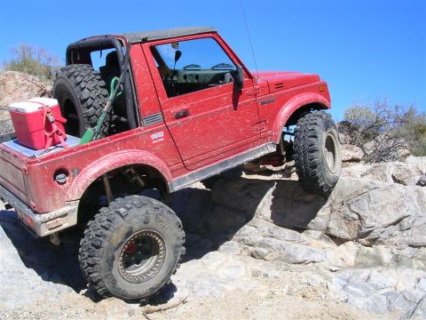 1987 Suzuki Samurai - This red 1987 Suzuki Samurai is tackling a rocky trail with its off-road tires.