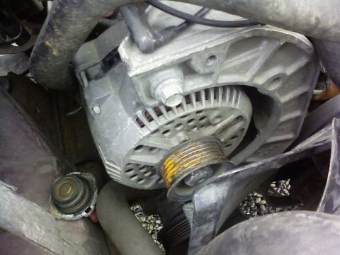 1995 Ford Bronco - This is a close-up view of a vehicle's alternator, showing its pulley and surrounding engine components.