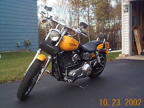1998 Ford Crown Victoria - A yellow Harley-Davidson motorcycle is parked outside a garage on a paved driveway.