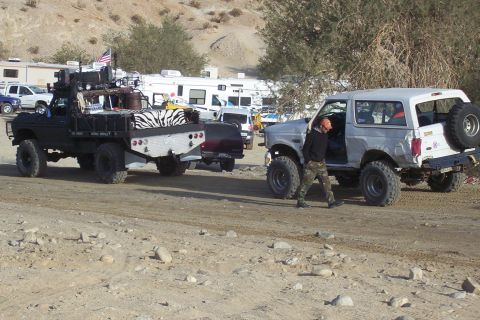 1995 Ford Bronco - A man exits a modified silver Ford Bronco parked on a dirt road with other vehicles and RVs in the background.