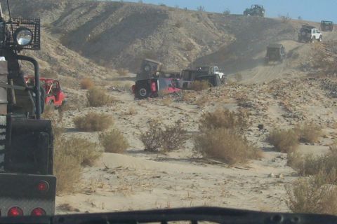 1995 Ford Bronco - Multiple off-road vehicles navigate a dusty, arid terrain with hills in the background.