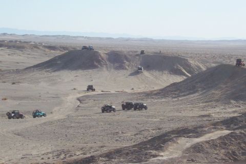 1995 Ford Bronco - Multiple off-road vehicles traverse a desert terrain with sandy hills under a clear sky.