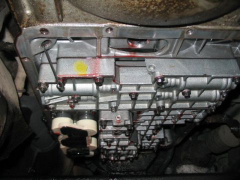 1991 Ford Bronco - Close-up of a vehicle's transmission valve body and pan, showing signs of fluid leakage.