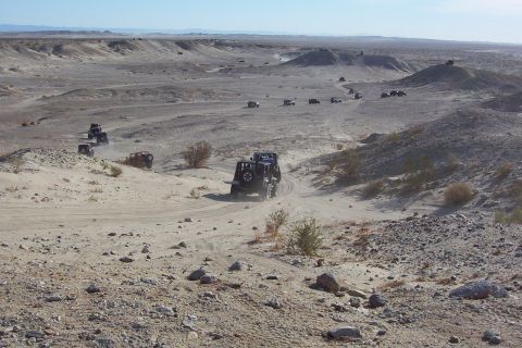 1995 Ford Bronco - A convoy of off-road vehicles traverses a dusty desert terrain, kicking up dust as they go.